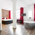 1st Floor Köln 2 in Cologne: stylish room with bed, red curtains, armchair and freestanding bathtub