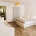 Pension George in Karterados, a bright guest room with a double bed, sofa, and herringbone wood floor.