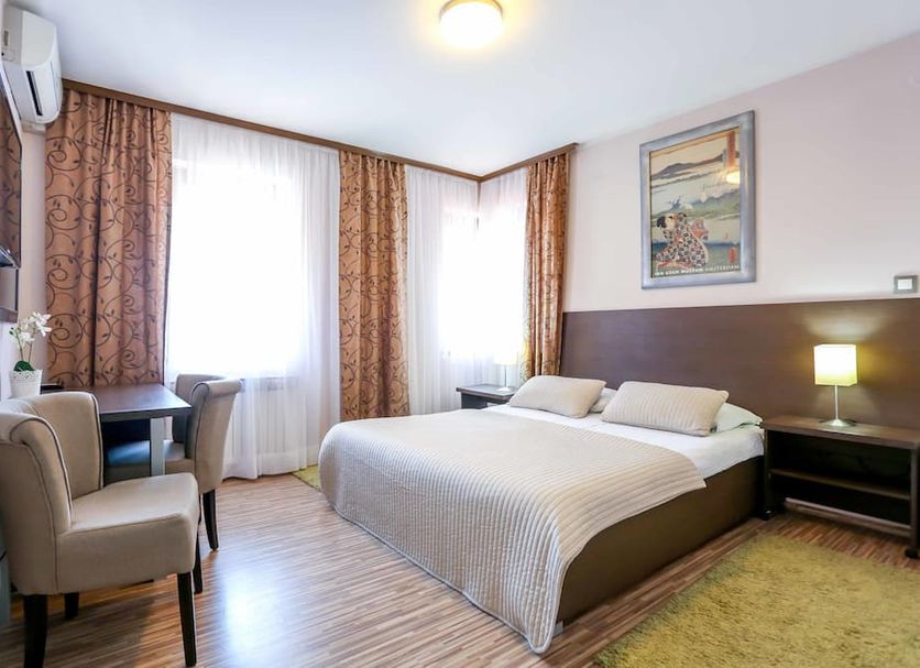 Hotel Divan Sarajevo guest room with double bed, armchair, desk, and windows with curtains