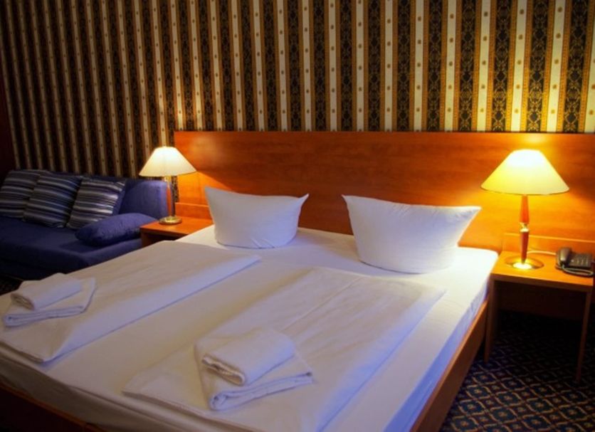 City Hotel am Kurfürstendamm, Berlin: double bed with bedside lamps and striped sofa in guest room