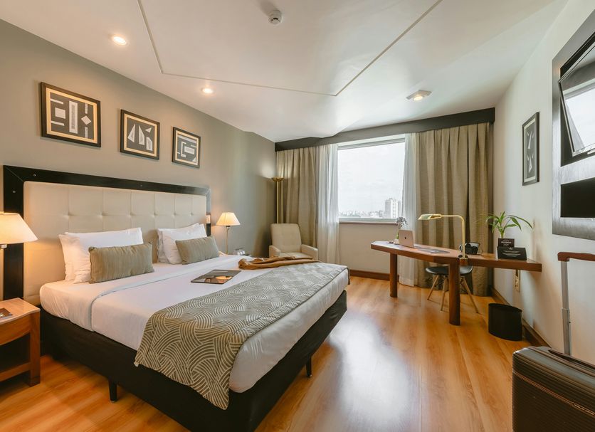 Pestana São Paulo guest room with king bed, desk, armchair and large window in São Paulo