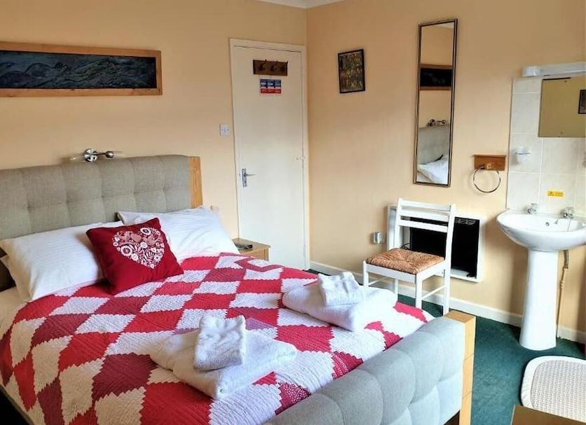 Avoncourt Lodge in Ilfracombe guest room with double bed, red quilt, sink and wall mirror