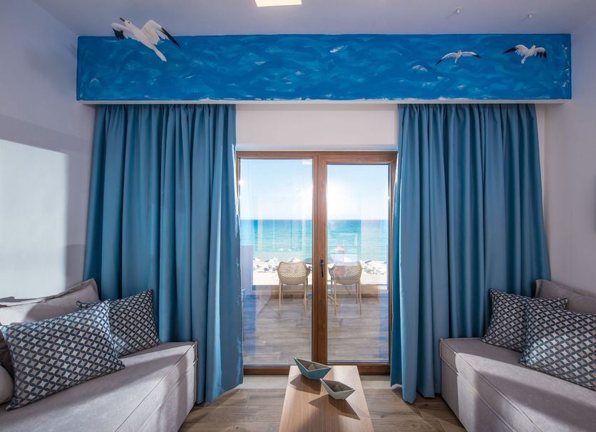 Yianna Caravel Suites in Gázi: sea-view room with balcony, blue curtains, and twin sofas