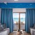 Yianna Caravel Suites in Gázi: sea-view room with balcony, blue curtains, and twin sofas