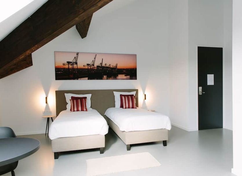 Trust Hotel Beveren guest room with twin beds, sloped ceiling and industrial wall art