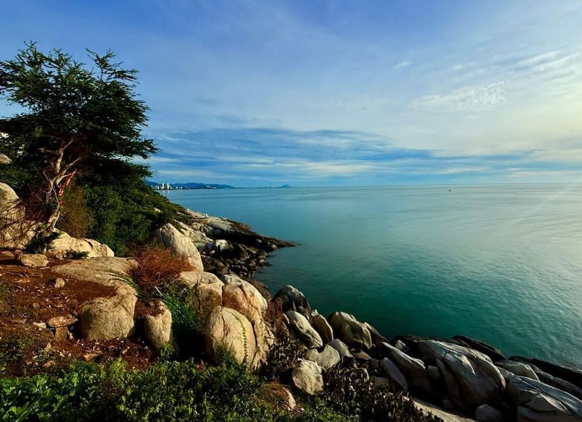 Luna Hut Resort Hua Hin rocky seaside view with calm ocean and tree-lined shore