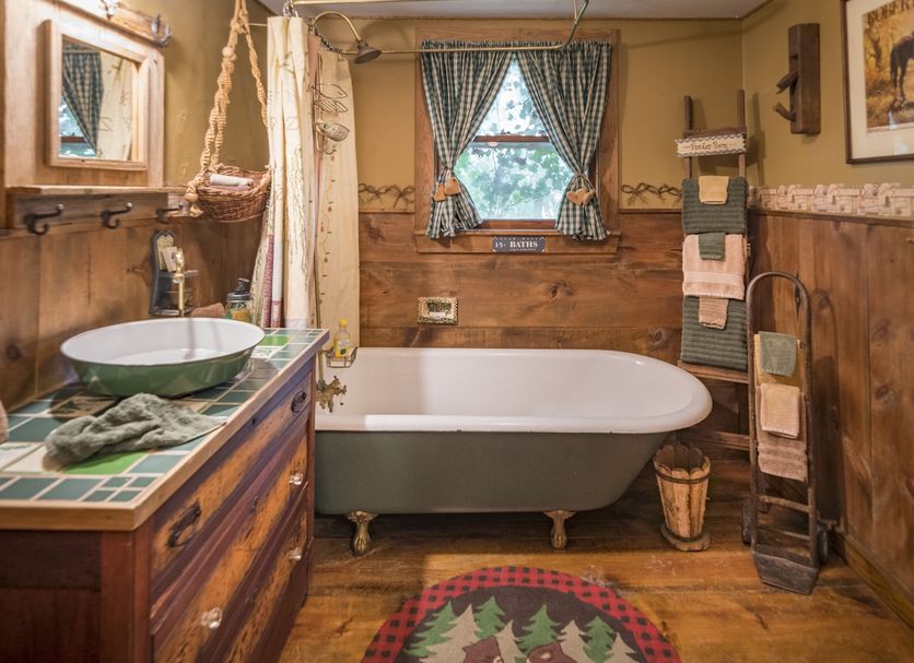 Country Woods Inn Glen Rose rustic bathroom with clawfoot tub, wood paneling, patterned curtains and vanity