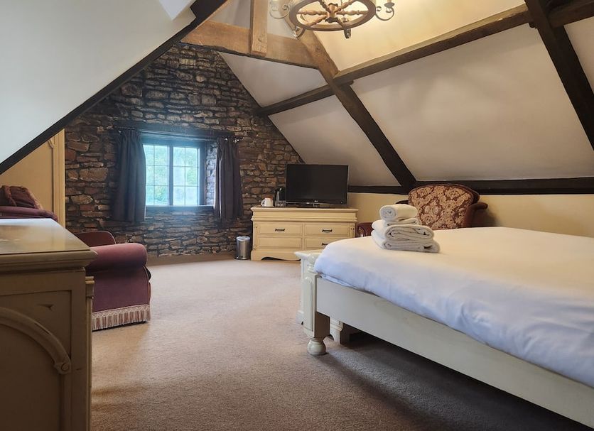 Langley Inn Bristol attic guest room with bed, TV, stone wall, and exposed beams