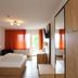 Alpina Löwen Hotel, Sankt Märgen: bright guest room with bed, orange curtains, wardrobe, and window view.