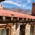 Refugio Del Pintor in Tilcara with stone roof, rustic facade, mountains and tree under blue sky