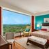 The Oberoi New Delhi guest room with large window views over greenery and a bright turquoise accent wall.
