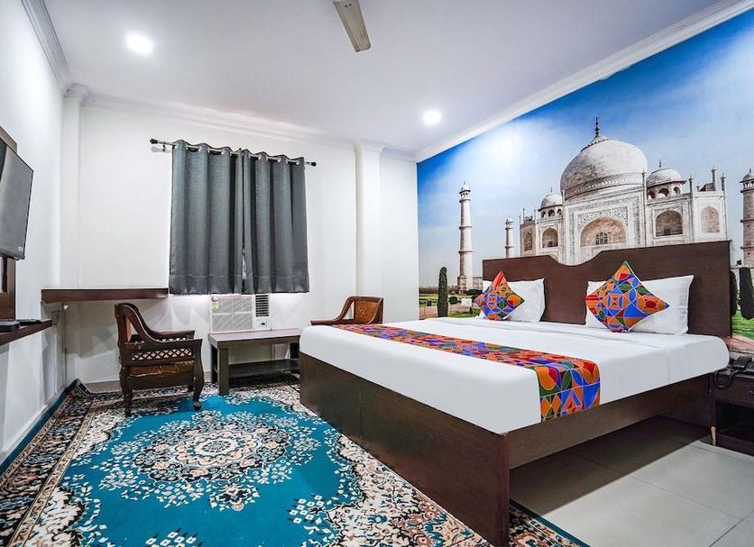 Hotel Taj Heritage in Agra guest room with king bed, colorful bedding, wall art of the Taj Mahal, and seating area