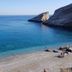 Vrahos Boutique Hotel in Folegandros overlooks a clear blue cove with a pebble beach and rocky cliffs.
