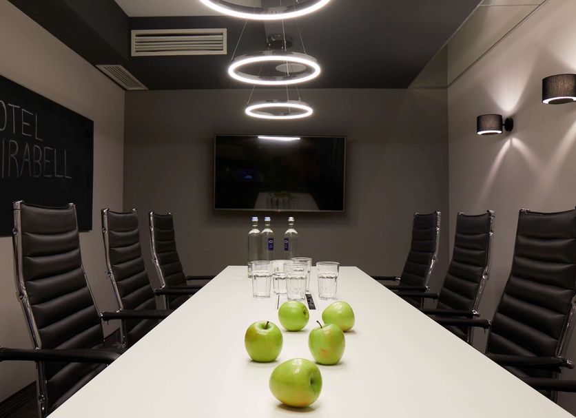 Hotel Mirabell München meeting room with long conference table, black chairs, and wall-mounted TV in Munich