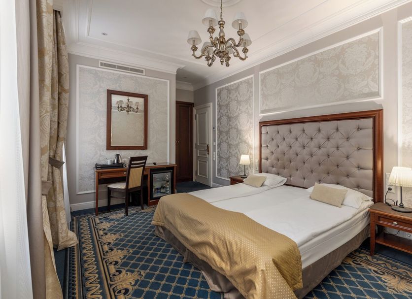 Gertrude Hotel self check-in in Riga: elegant double room with tufted headboard, desk, chandelier, and patterned carpet
