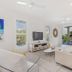 Metzo Noosa Resort living room with white sofa, TV stand, beach art and tropical balcony view in Noosa Heads