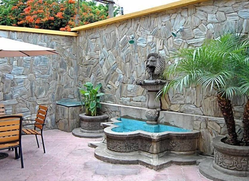 Hostal Los Volcanes, Guatemala City: stone courtyard with fountain, patio table, umbrella and potted palms