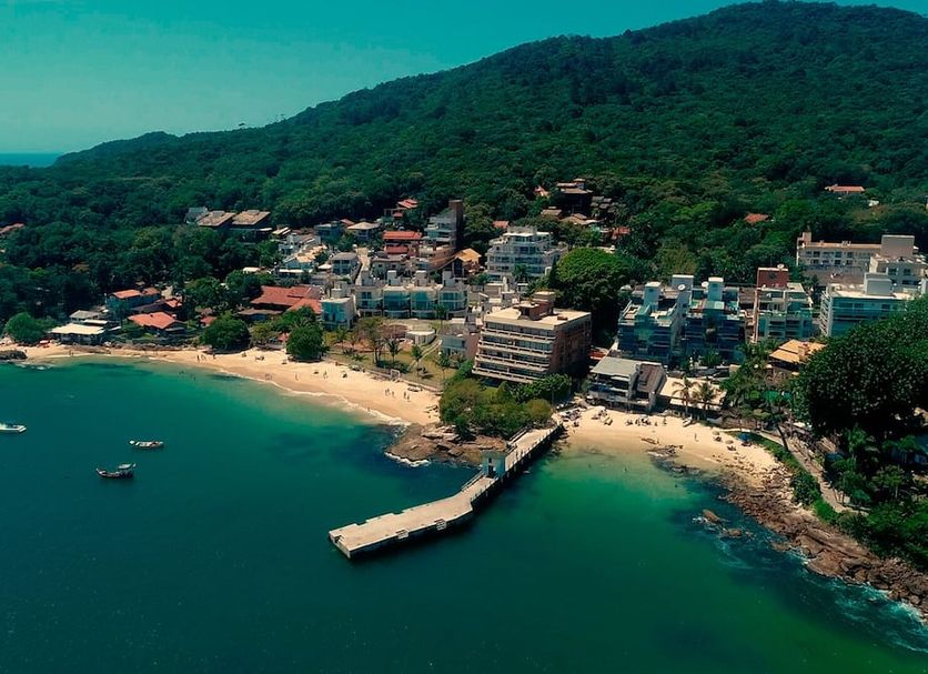 Pousada Palmeiras in Bombinhas with beachfront bay view, sandy beach, pier and hillside resort buildings