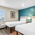 Woodspring Suites San Antonio South guest room with two beds, teal accent wall and window