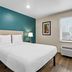 Woodspring Suites San Antonio South room with king bed, teal accent wall, window and air conditioner in San Antonio