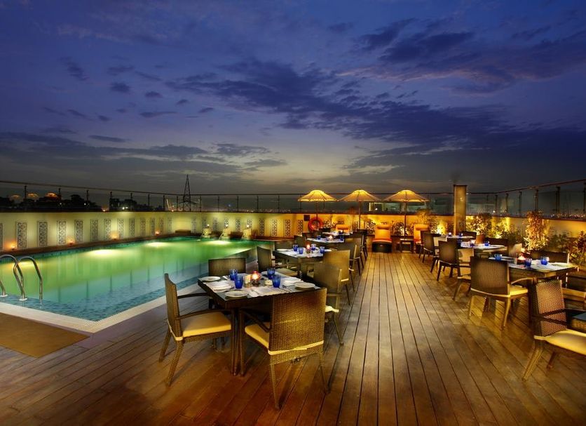 Mahagun Sarovar Portico Suites Ghaziabad rooftop pool deck with dining tables at dusk