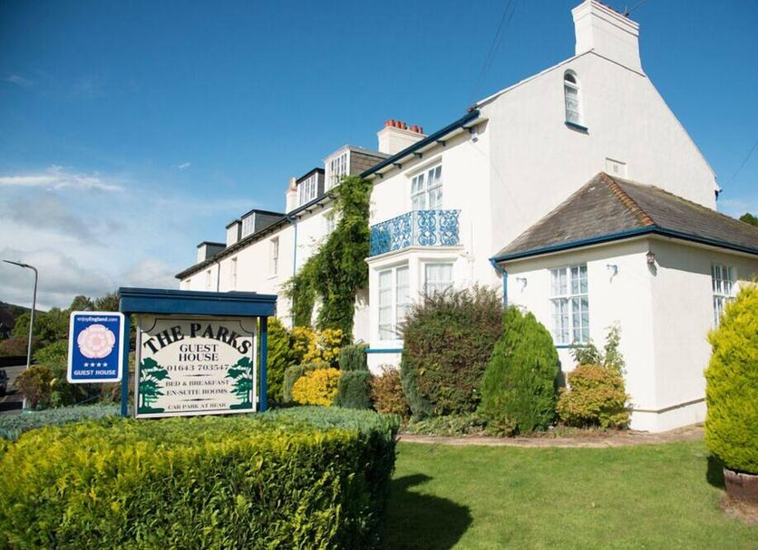 The Parks Guest House in Minehead, exterior view with white facade, garden hedges and sign