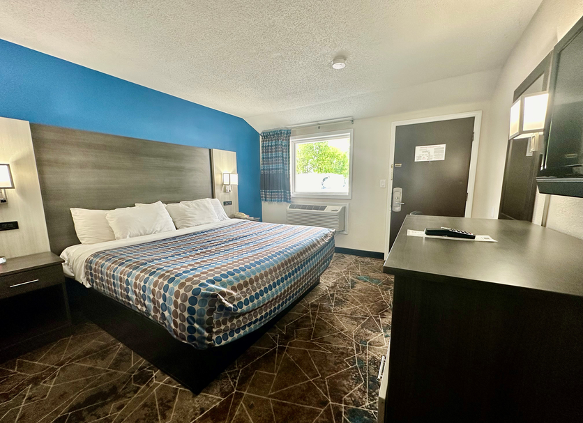 Red Carpet Inn Orchard Park guest room with king bed, TV, desk, and window in Orchard Park