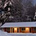 North Creek Lodge at Gore Mountain in North Creek, snow-covered lodge cabin at dusk with lit windows and trees
