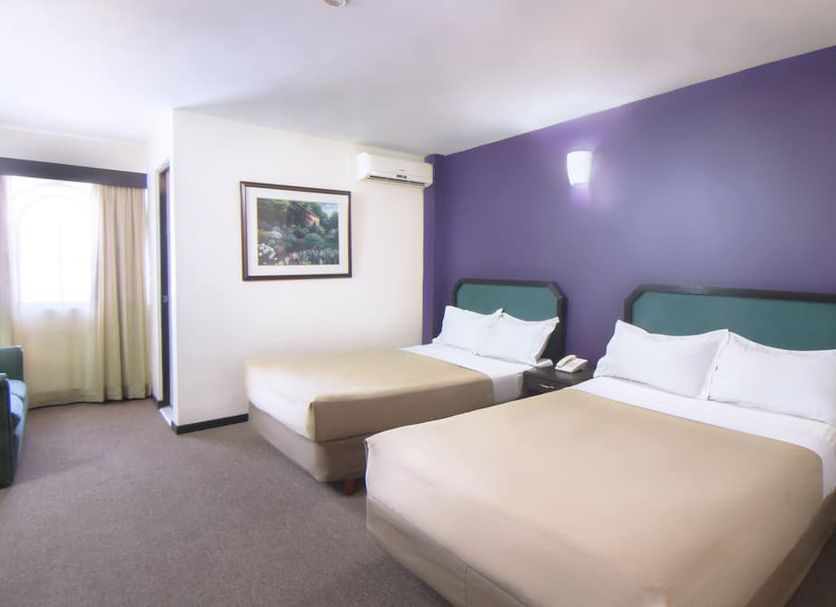 Chn Hotel Monterrey Santa Fe guest room with two beds, purple accent wall, and window with curtains