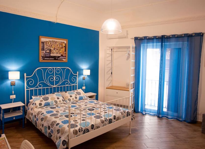 Quattro Incanti Palermo guest room with blue accent wall, double bed, and balcony doors with sheer curtains