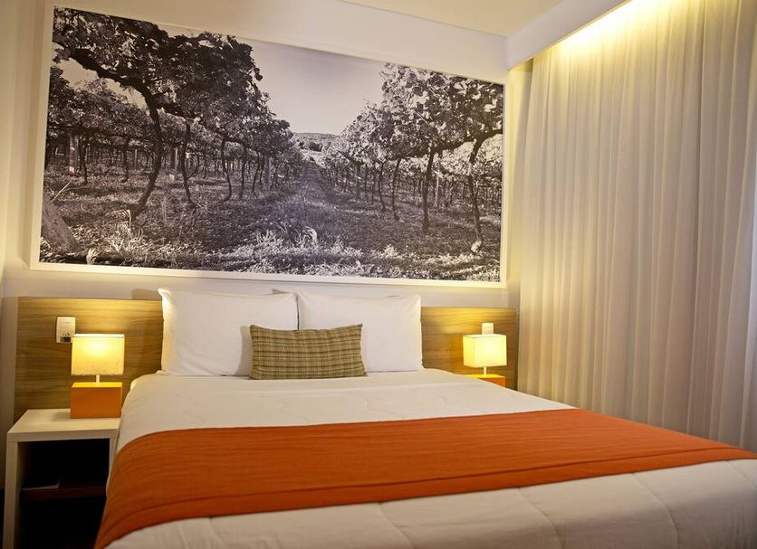 Partner Caxias do Sul room with king bed, bedside lamps, and large framed landscape wall art