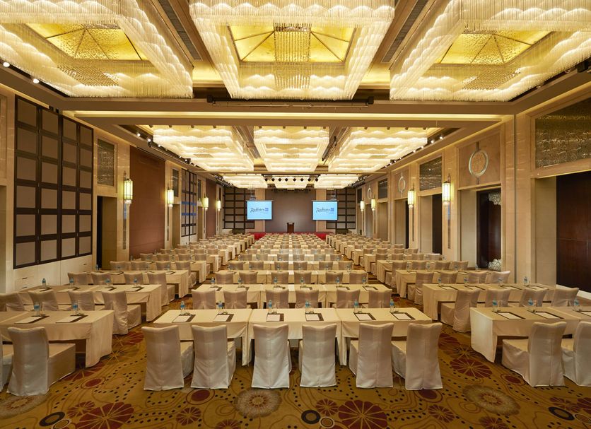 Radisson Blu Hotel Liuzhou banquet hall with rows of round tables and chairs under a bright patterned ceiling