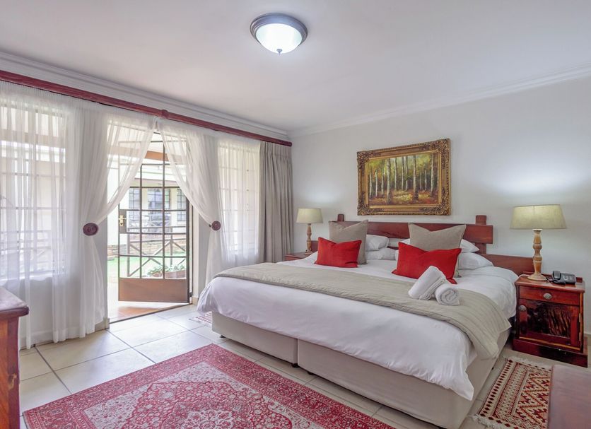 Afrique Boutique Hotel O.R. Tambo guest room with king bed, red accents, balcony doors and forest artwork in Boksburg