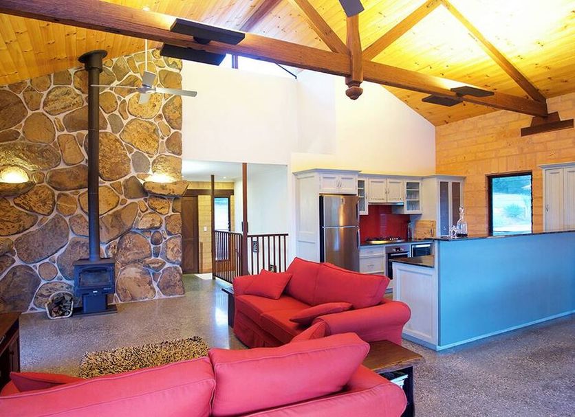 Clarendon Forest Retreat Forster cabin interior with stone fireplace, kitchen, and red sofas