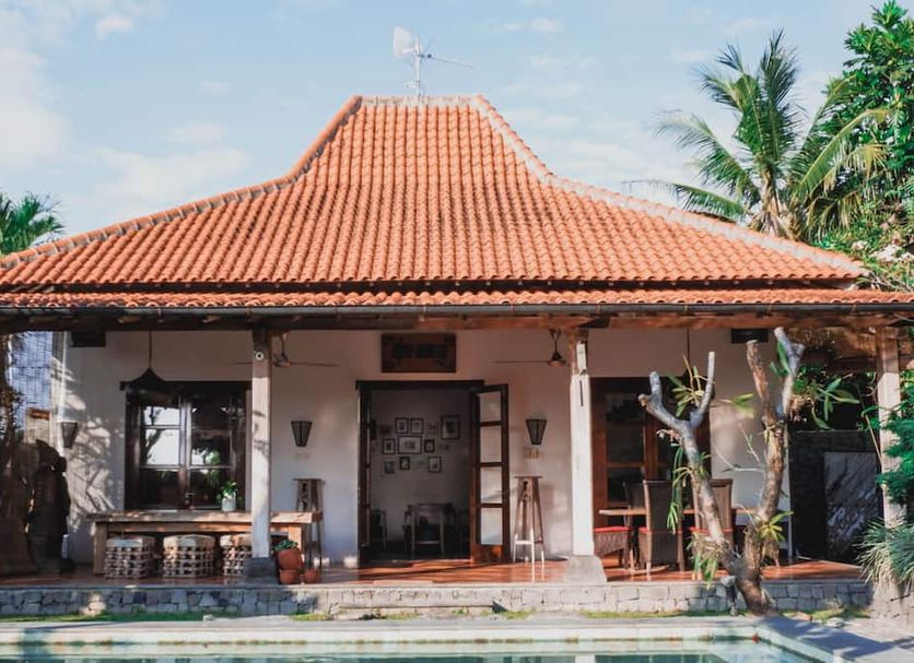 Villa Aquin in Colomadu, traditional villa with terracotta roof and front porch surrounded by palm trees