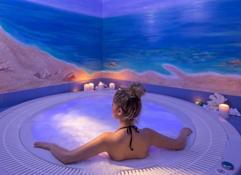 Princess Kyniska Suites Monemvasia spa with woman relaxing in indoor hot tub and blue sea mural