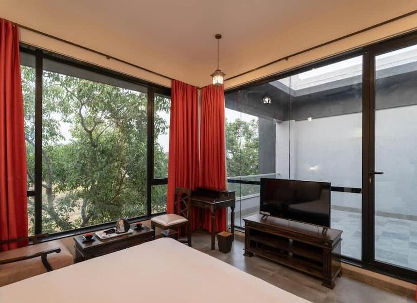 Triose Boutique Hotel Lonavala room with large windows, red curtains and a TV, overlooking greenery