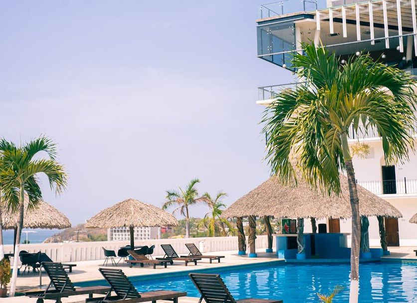 Hotel Caracol Plaza in Puerto Escondido with pool, palm trees, thatched umbrellas and ocean view