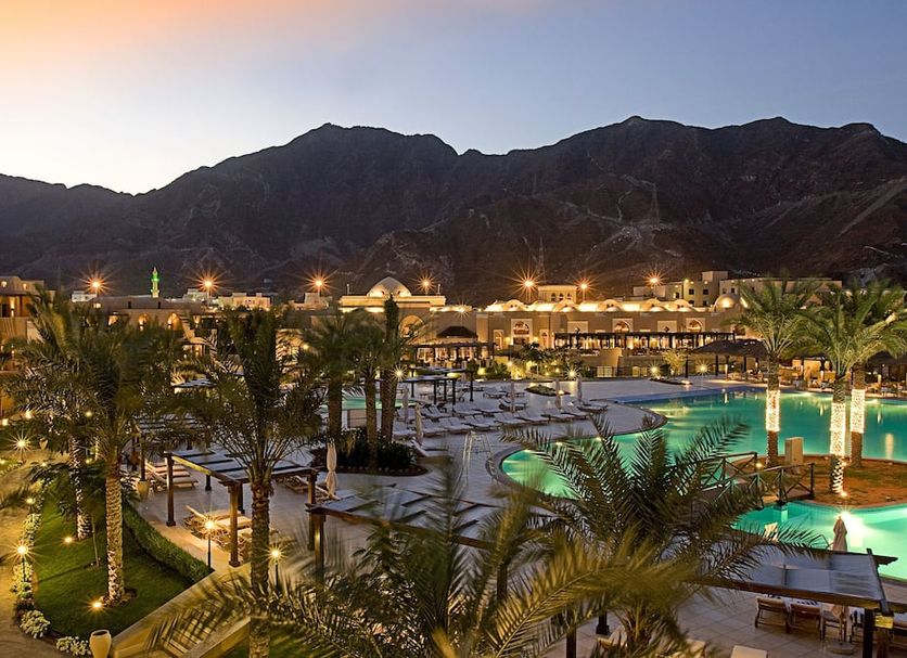 Miramar Al Aqah Beach Resort in Dibba Al-Fujairah with lit pools, palm trees and mountain backdrop