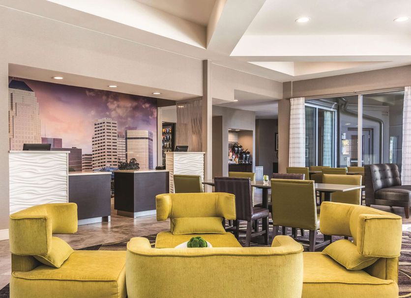 La Quinta Inn & Suites by Wyndham Shreveport Airport lobby lounge with yellow chairs and city mural