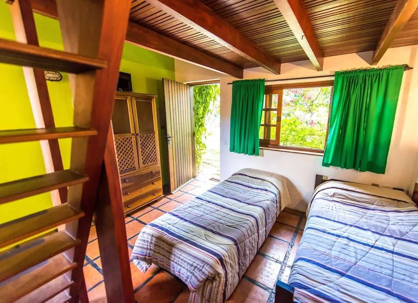 Pouso Sambaquis in Ilhabela with two single beds and a wooden loft ladder in a bright guest room