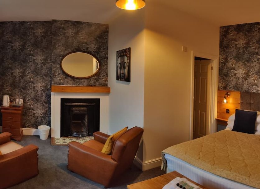 The Mansion in Whitehaven: guest room with fireplace, leather chairs and a bed beside an alcove wall light