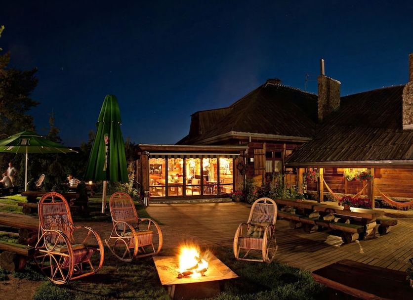 Karczma Rzym in Bydgoszcz with a lit fire pit, wicker chairs and a warmly lit outdoor terrace at night