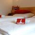 First Mountain Montafon in Gaschurn: neatly made twin beds with red pillows and branded cards in a simple room.