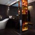 QT Sydney, Sydney: stylish bathroom with freestanding white tub, dark tile walls, and lit glass shelving
