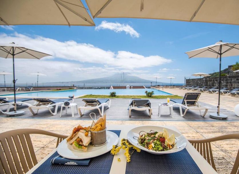 Azoris Faial Garden in Horta with terrace dining, poolside loungers, umbrellas and ocean and mountain views