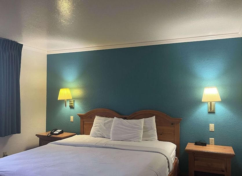 Motel 6 Portland, IN guest room with king bed, teal accent wall, bedside lamps and nightstands