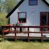 Grindsted Aktiv Camping cabin with a wooden deck, red-trim windows and a seated guest in Grindsted