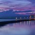 The Sarojin in Takua Pa with a lit pier over calm water at dusk and a purple sky