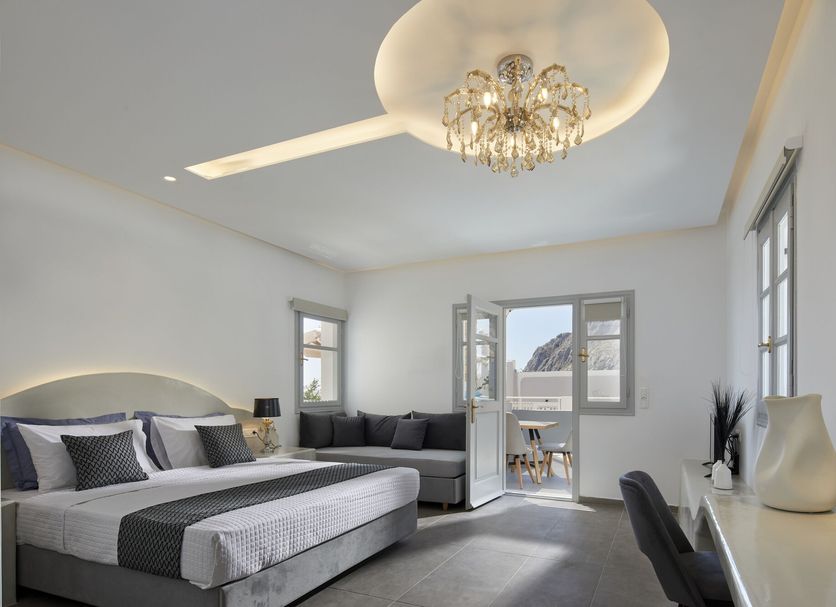 Blue Sea Hotel Kamari bedroom with king bed, sofa, chandelier and balcony door to sea view